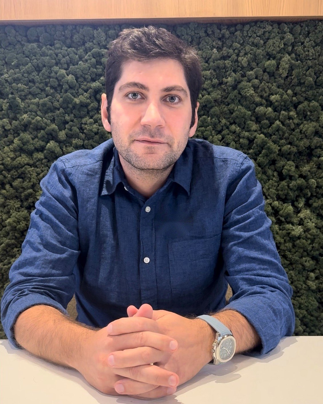 Baturay Özden, seated at a table in front of a green moss wall